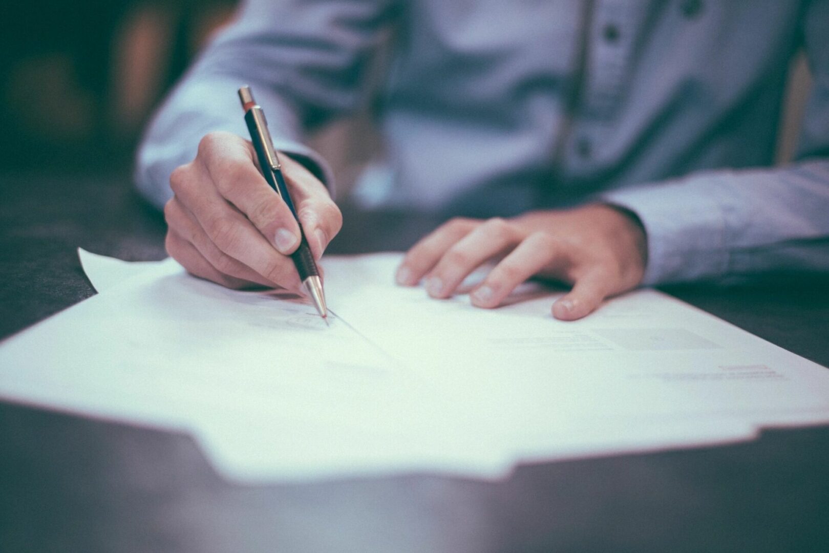 Person writing on papers with a pen at a desk.
